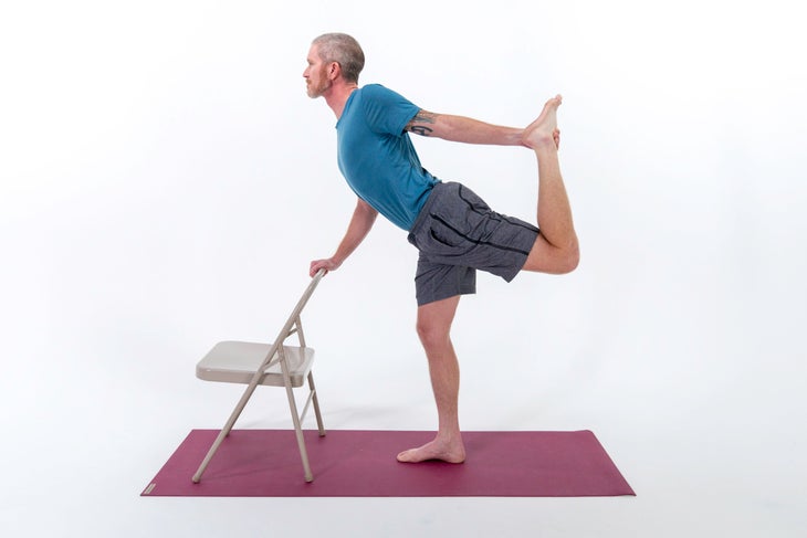 A person demonstrates a variation of Dancer Pose using the back of a chair