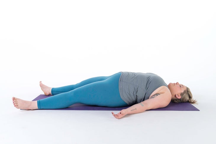 A woman lies in Corpse Pose (Savasana) in yoga