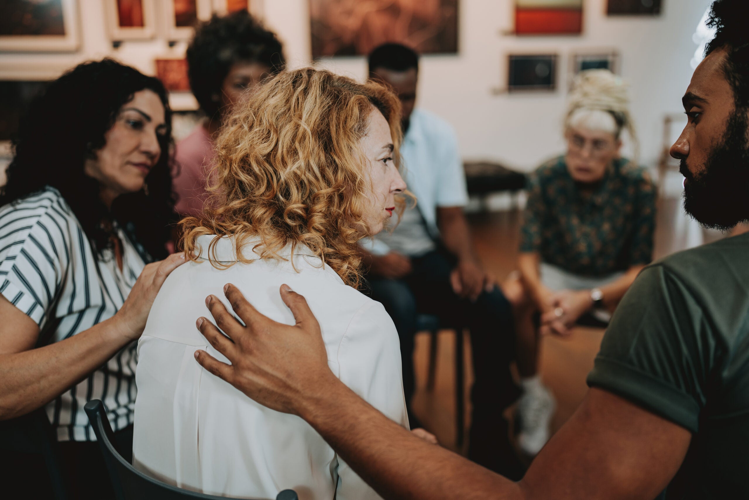 Woman sitting in a circle with other people supporting her.