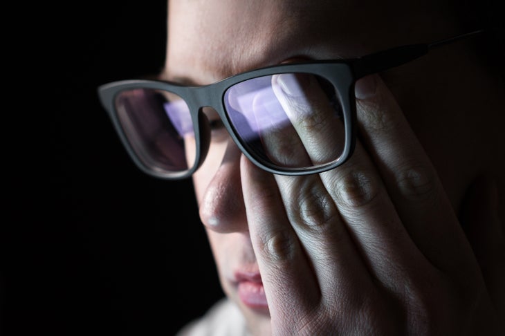 Man wearing dark-framed glasses rubbing tired eyes. Problem with glasses, eyesight or vision. Person having stress or depression. Workplace bullying. Working late with computer.