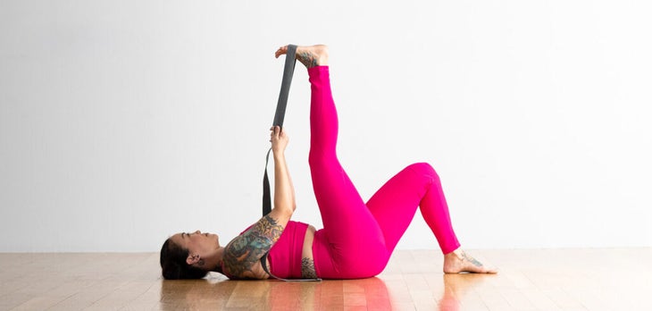 Woman lying on her back with one knee bent and one leg straight and a strap around her lifted leg to stretch her tight hamstrings