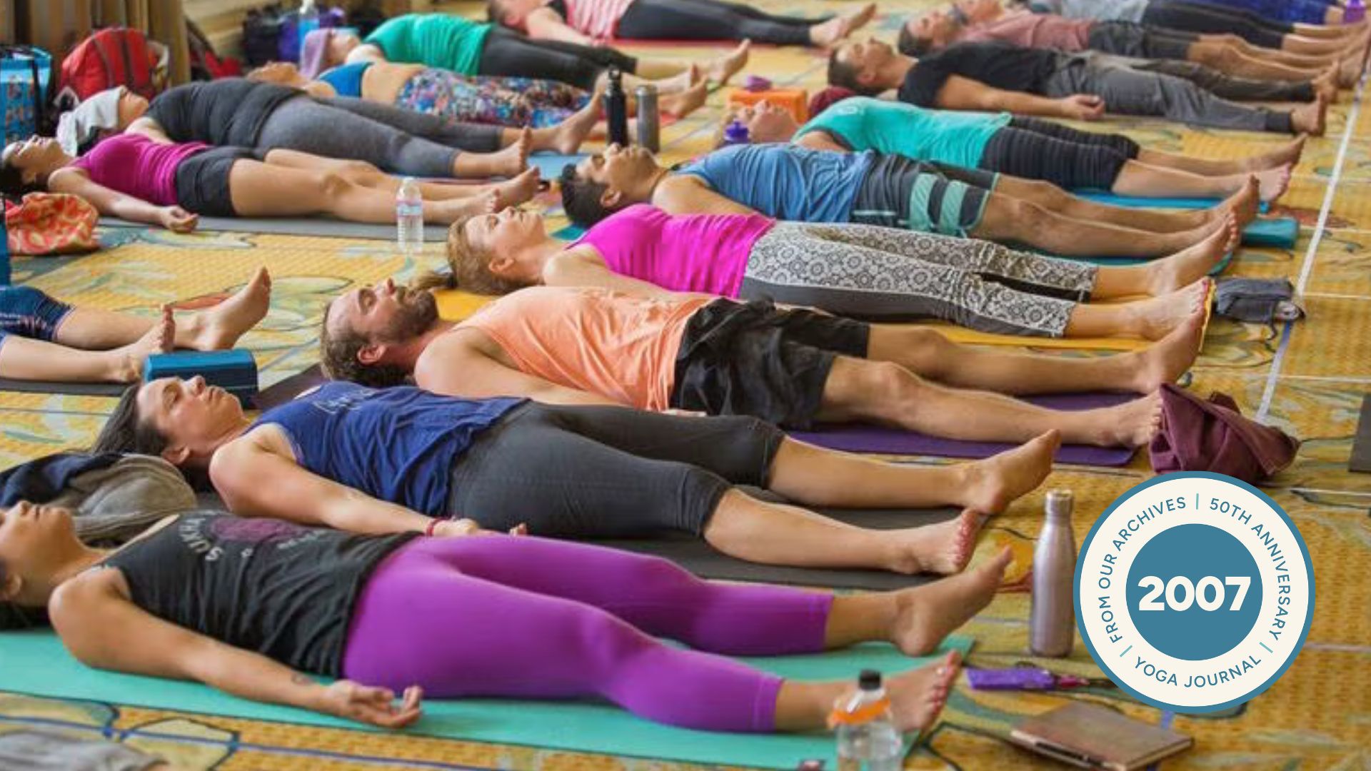 People wearing colorful clothing lying in Savasana.