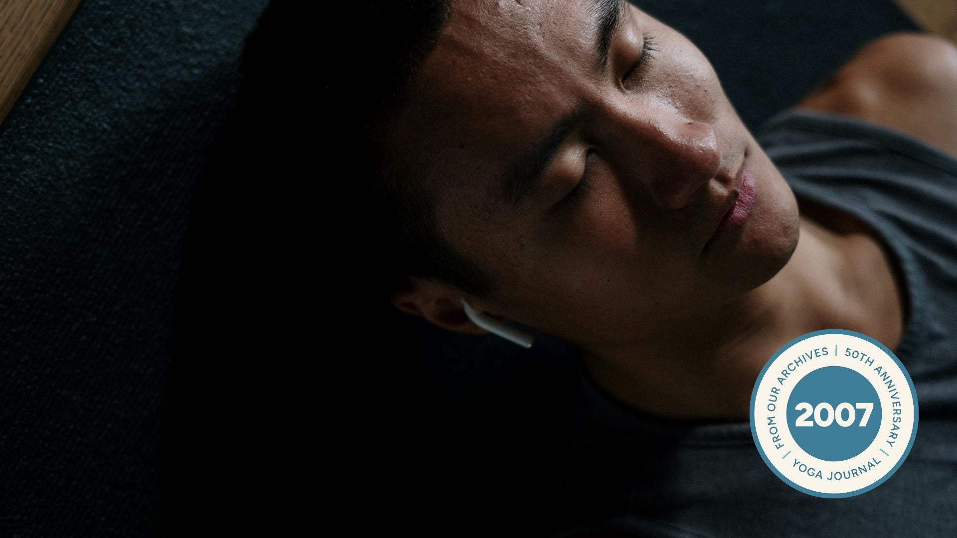 Man lying on yoga mat with eyes closed in dark room.