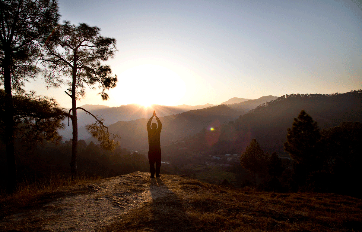 Man practicing Surya Namaskar or Sun Salutation A at sunrise in the mountains