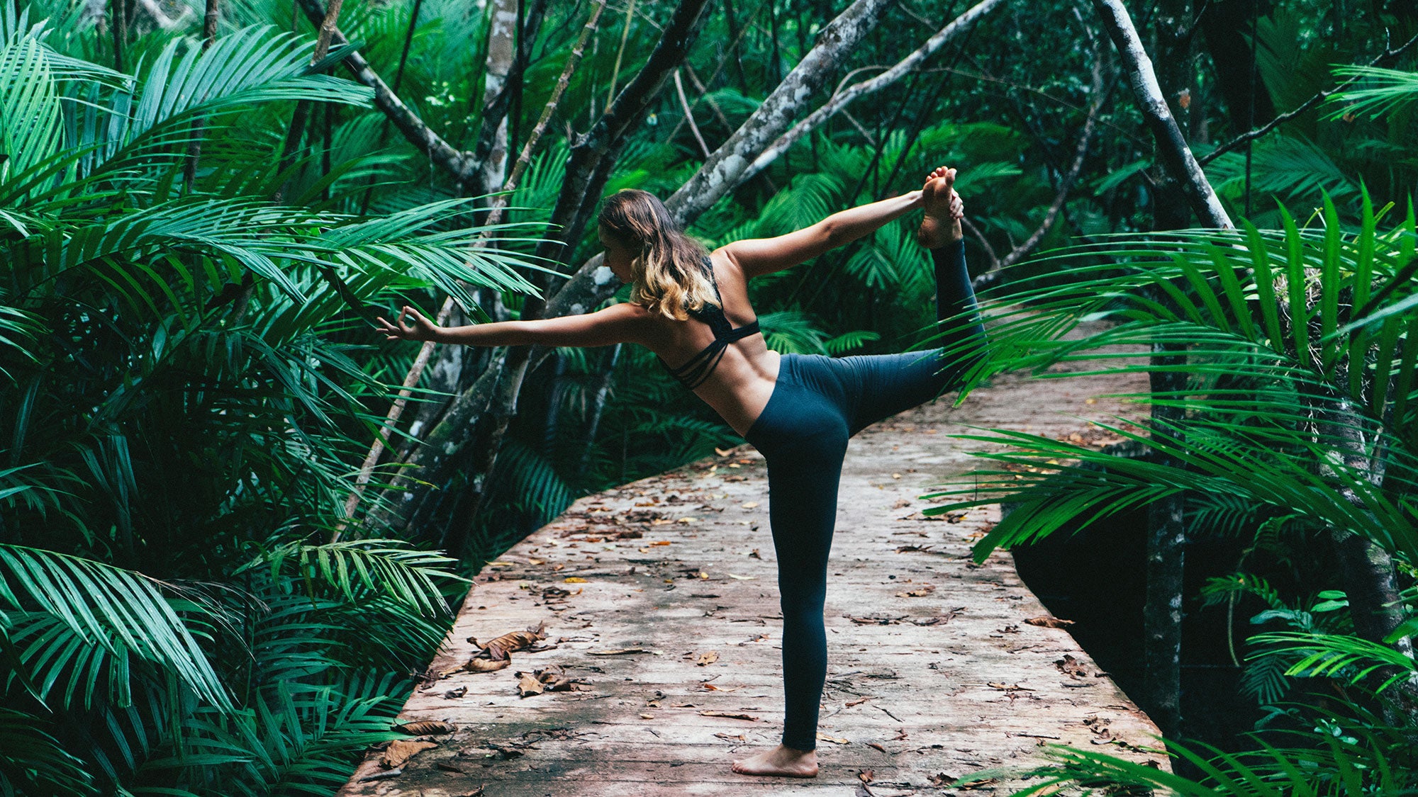 A woman demonstrates Dancer pose among palm trees