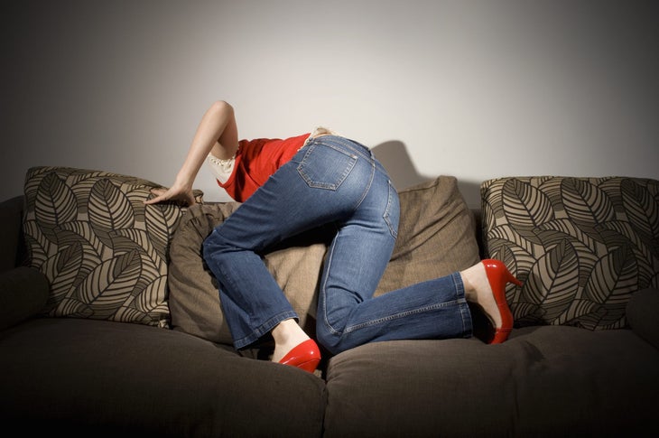 Person in red shirt and red heels looking behind sofa, rear view