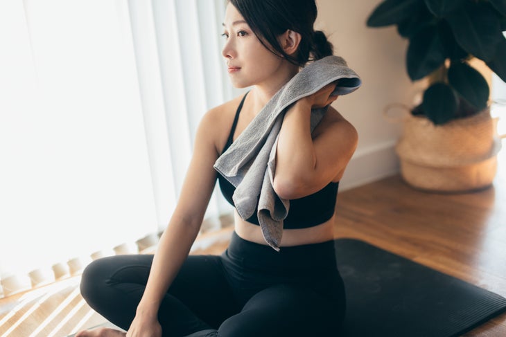 Woman wiping sweat off her neck with a towel after doing yoga.