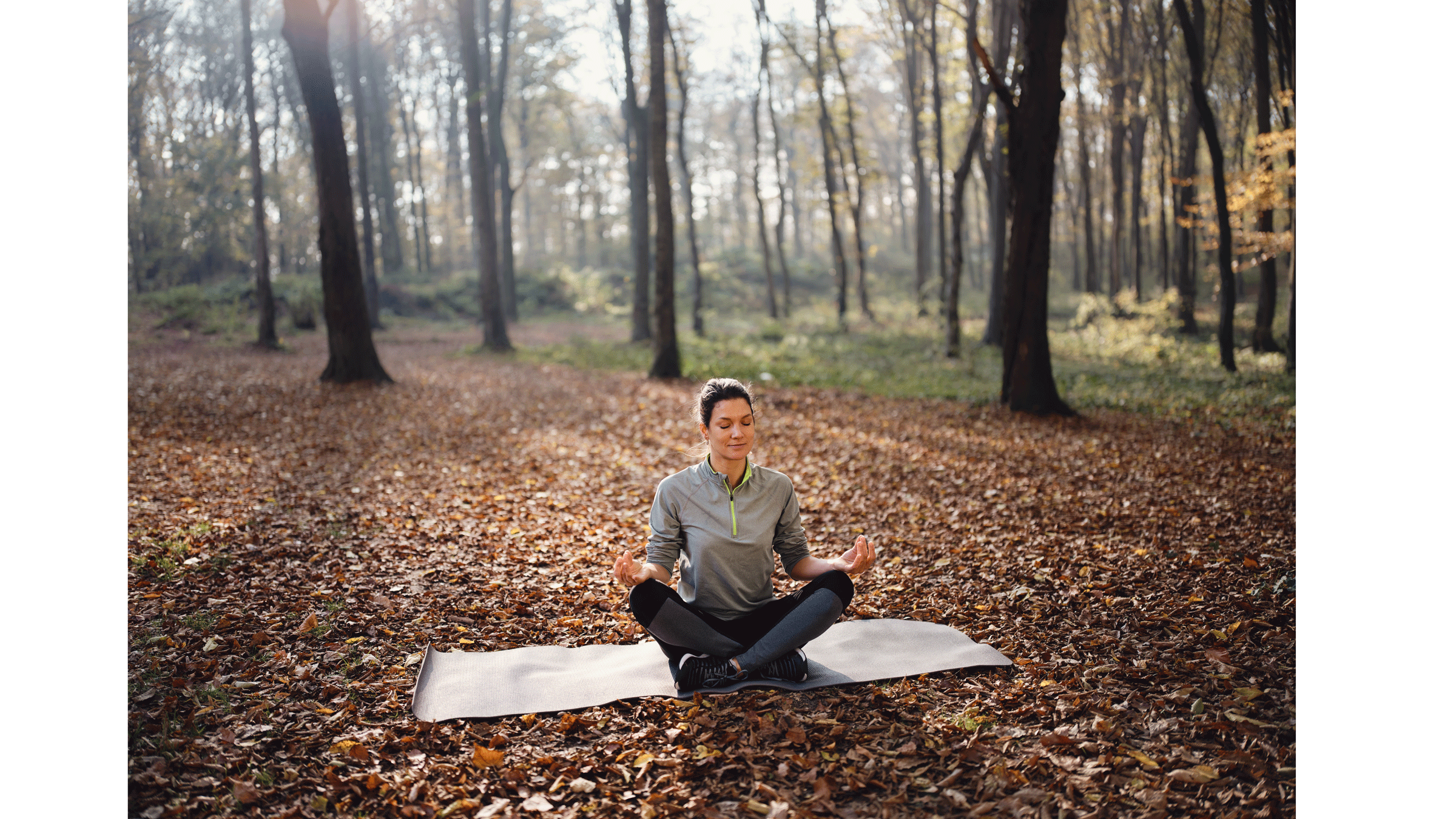 Woman sitting on a yoga mat outside among the changing leaves being calm