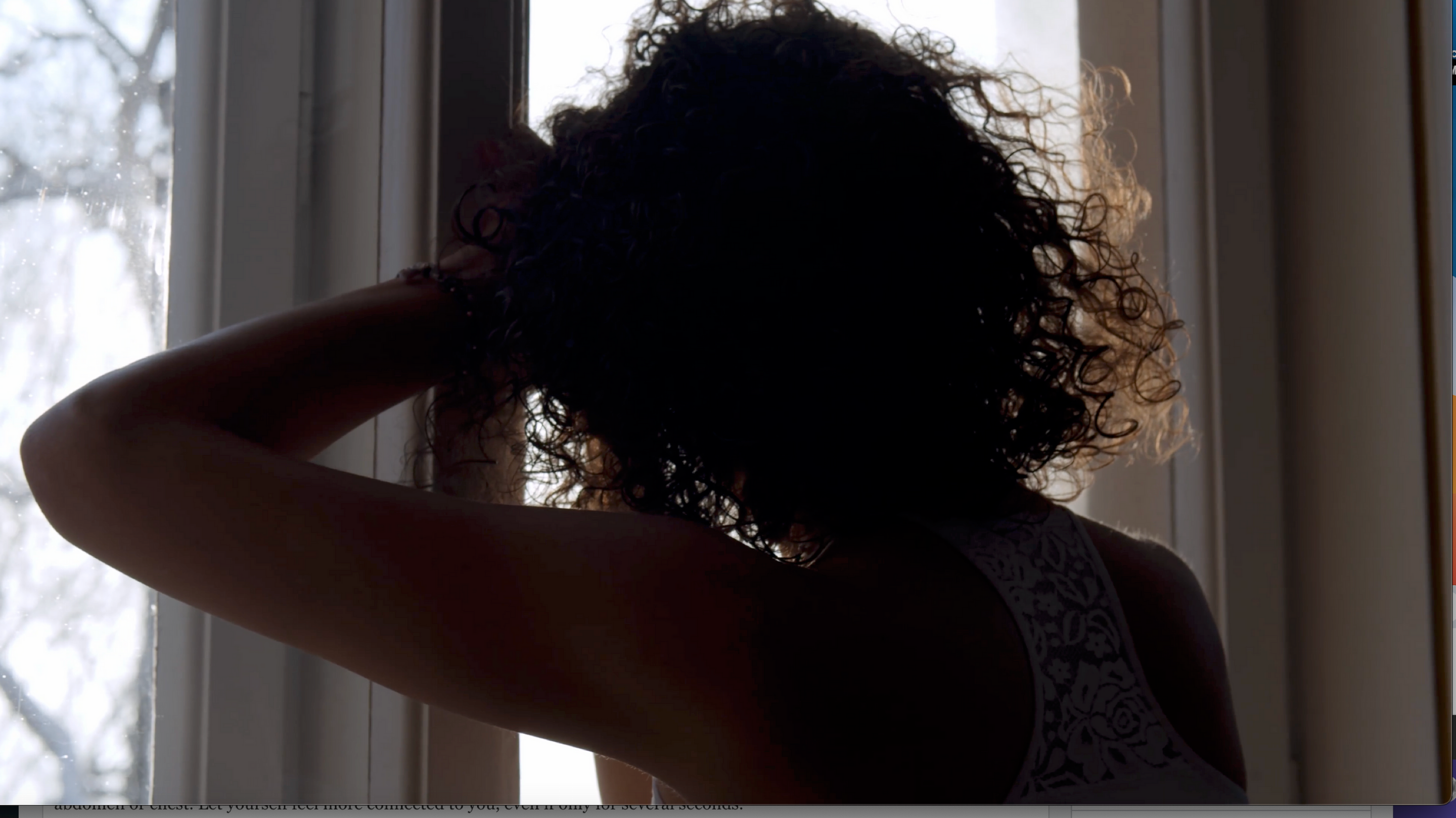 Woman leaning against a window with her back to the camera looking emotionally overwhelmed