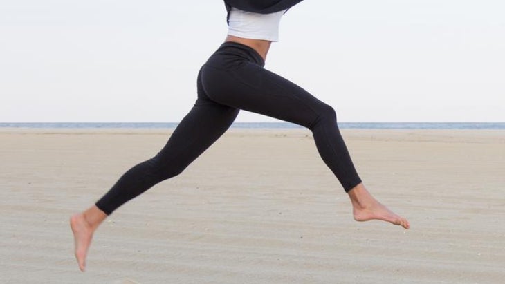 Closeup of leggings on woman mid-jump at the beach