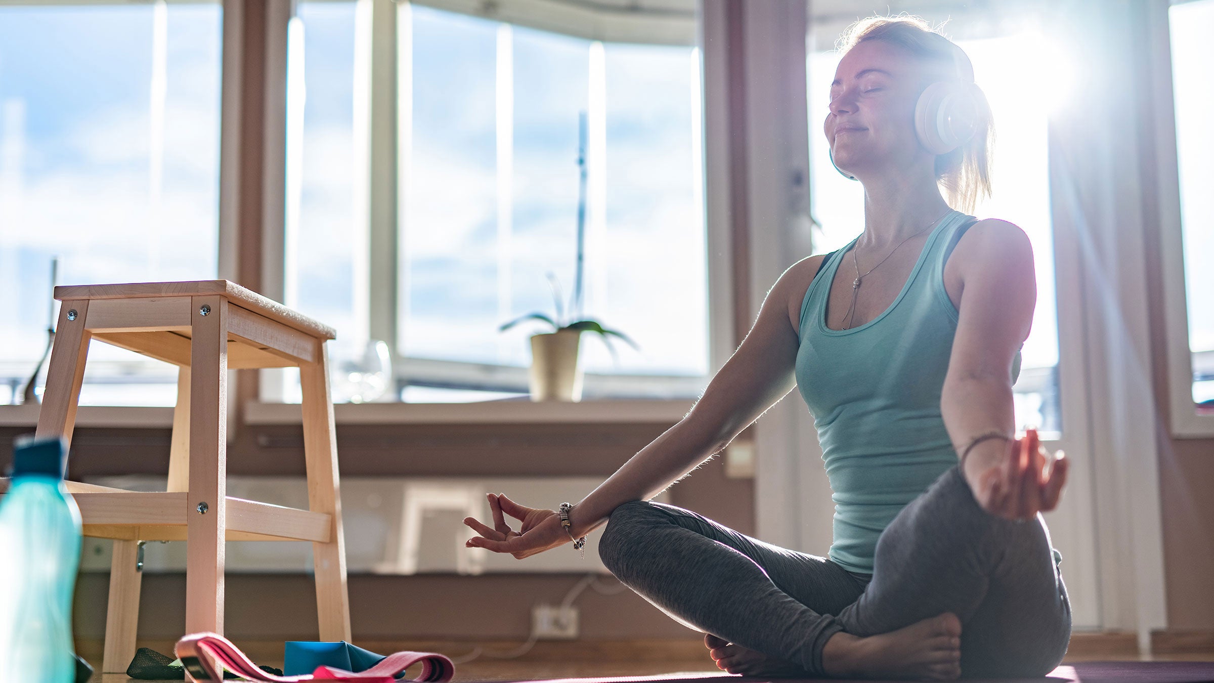 A woman sits on a yoga mat while listening to music on headphones