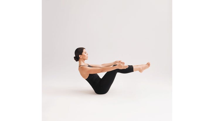 A woman wearing black demonstrates Ardha Navasana (Half Boat Pose) in yoga