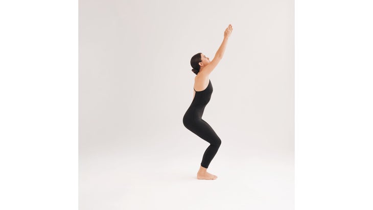 A woman wearing black demonstrates Utkatasana (Chair Pose) in yoga