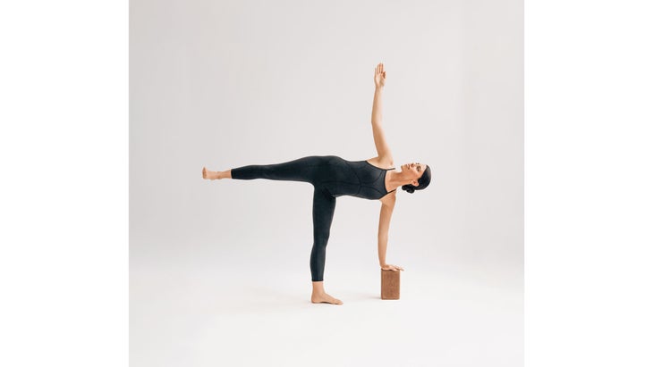 A woman wearing black demonstrates Ardha Chandrasana (Half Moon Pose) in yoga
