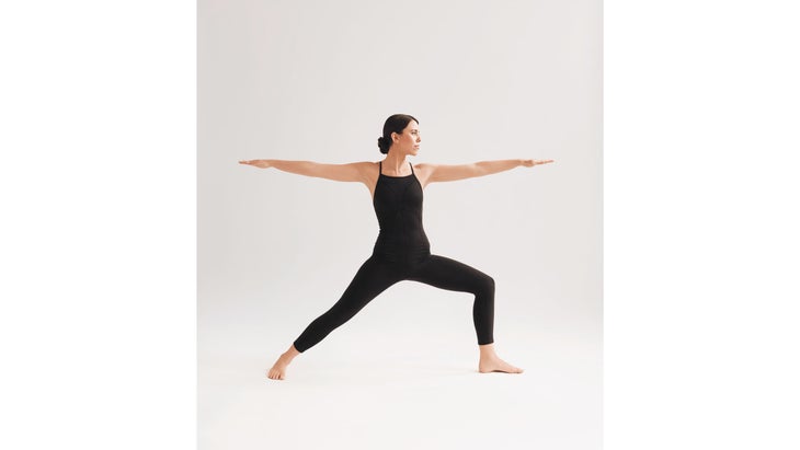 A woman wearing black demonstrates Virabhadrasana II (Warrior Pose II) in yoga