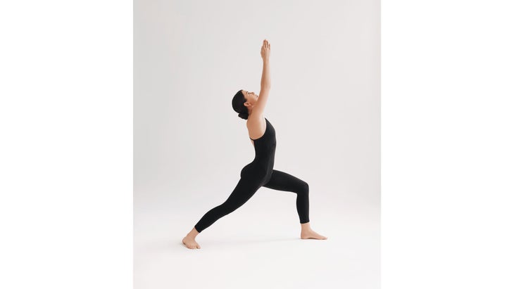 A woman wearing black demonstrates Virabhadrasana I (Warrior Pose I) in yoga