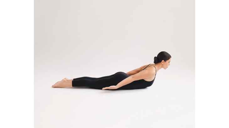 A woman wearing black demonstrates Salabhasana (Locust Pose) in yoga