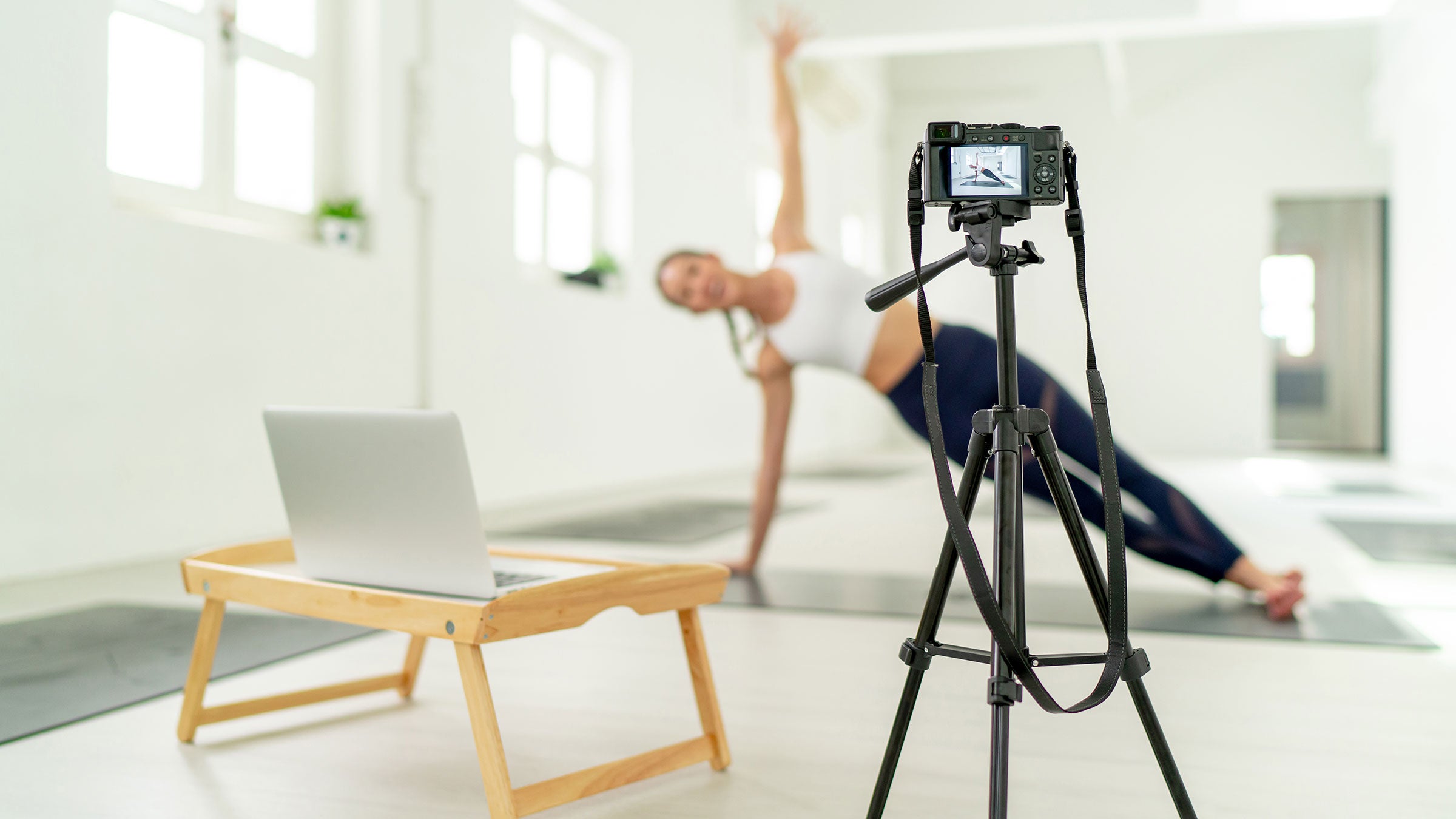 A woman demonstrates a yoga pose in front of a camera and computer