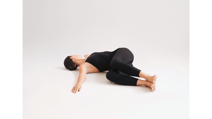 A woman wearing black demonstrates Jathara Parivartanasana (Revolved Abdomen Pose) in yoga