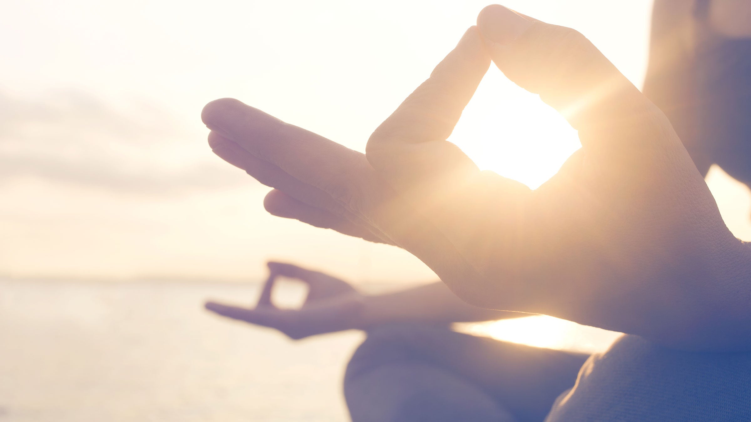 A person sits with their thumb and pointer fingers together at sunset