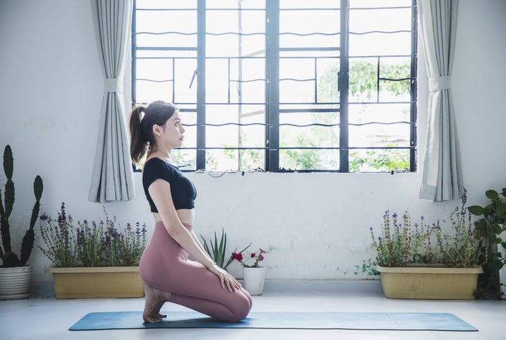 Young Asian woman in Black top and pink pants knees in Thunderbolt pose