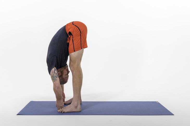 Man in red shorts folding into Hasta Padangustasana (Big Toe Pose)