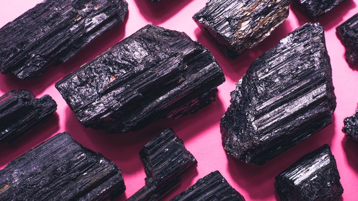 Black tourmaline crystals are pictured on a pink background