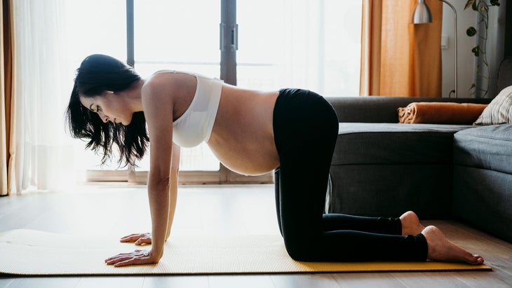 A pregnant woman demonstrates Tabletop pose in yoga at home