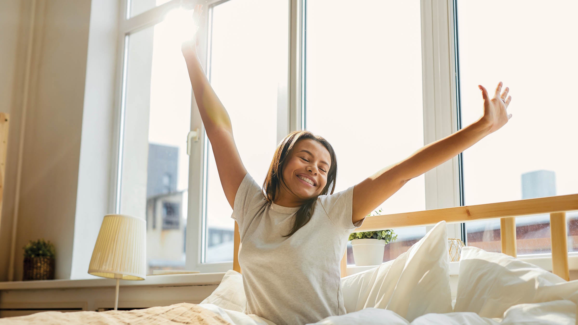 Mixed-Race woman stretching, sitting in bed lit by sunlight