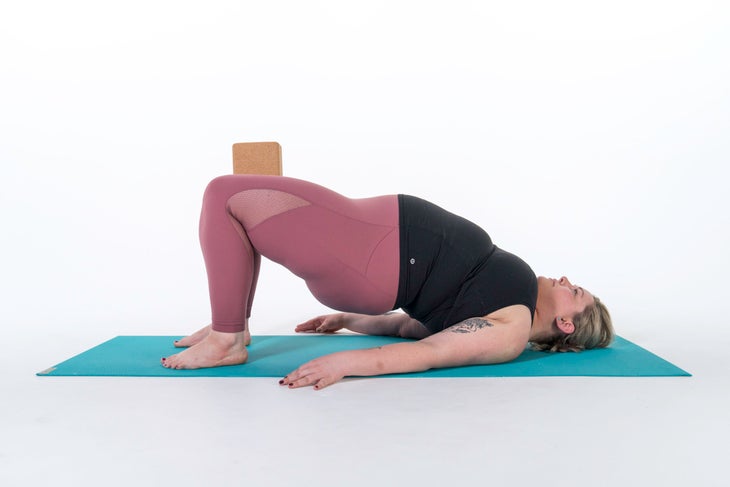 A person demonstrates a variation of Bridge Pose (Setu Bandha Sarvangasana) with a block between their knees