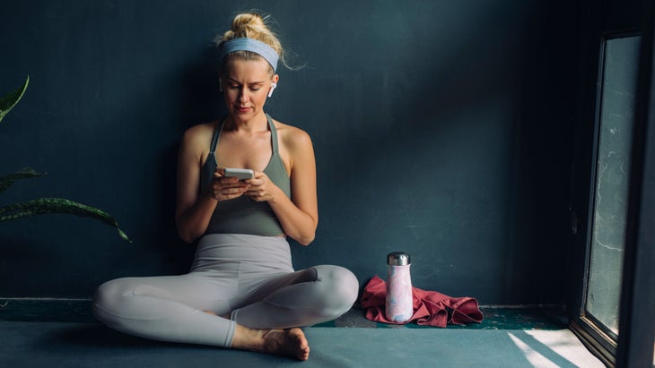 Woman looks at her phone while on a yoga mat