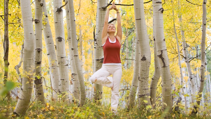 A woman demonstrates Tree Pose among aspen trees during the fall season