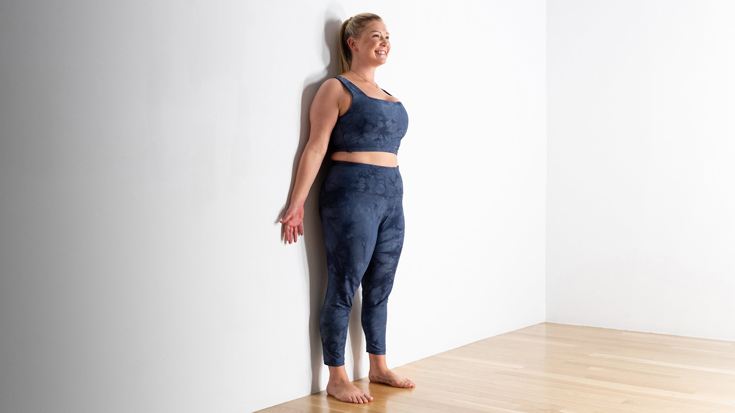 Woman in a Mountain Pose variation against a wall