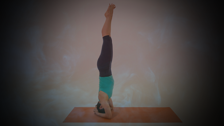 Woman does supported headstand on an orange mat.