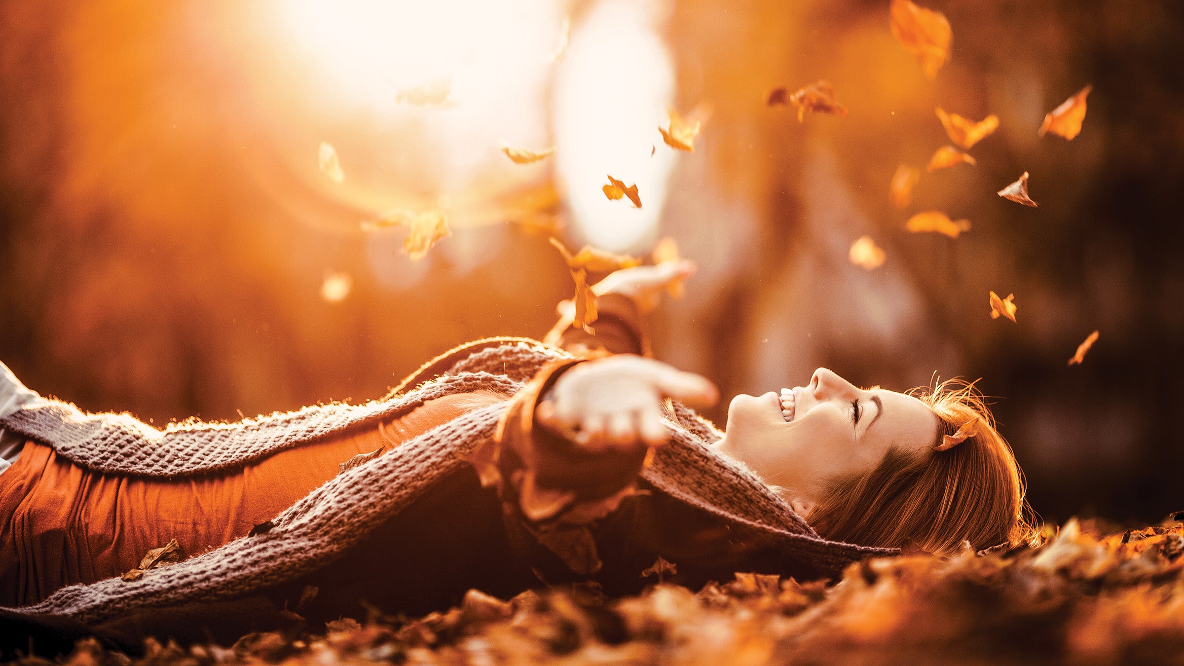 Woman lying on her back, throwing leaves in the air
