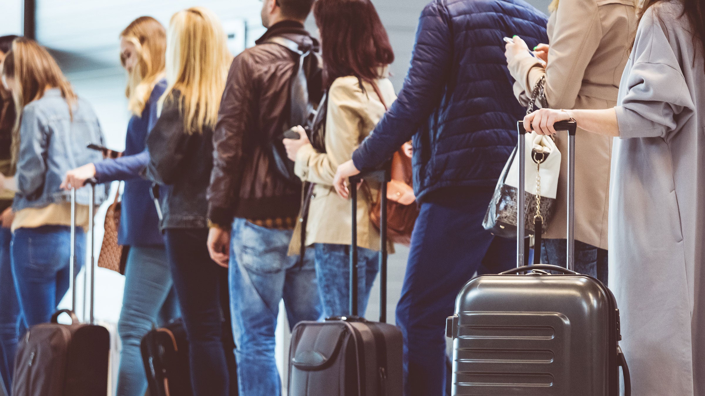 People wait in line with their luggage at an airport
