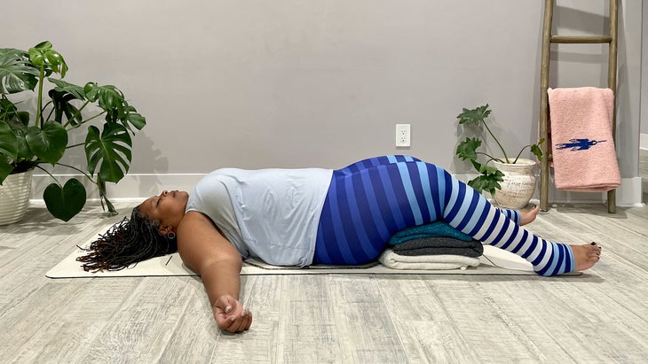 A person demonstrates supported Savasana (Corpse Pose) in yoga