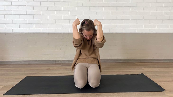A person curls their fingers inward and pulls their forearms toward their head in yoga