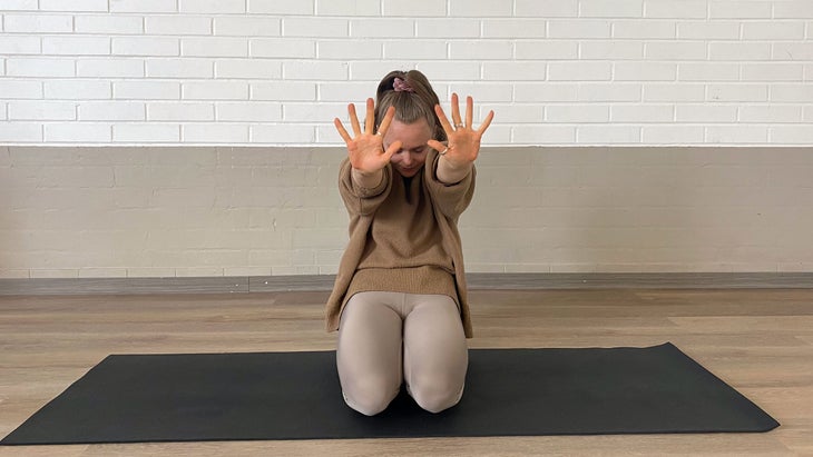 A person pushes their palms forward from their ears while rounding gently through their back in Yin Yoga