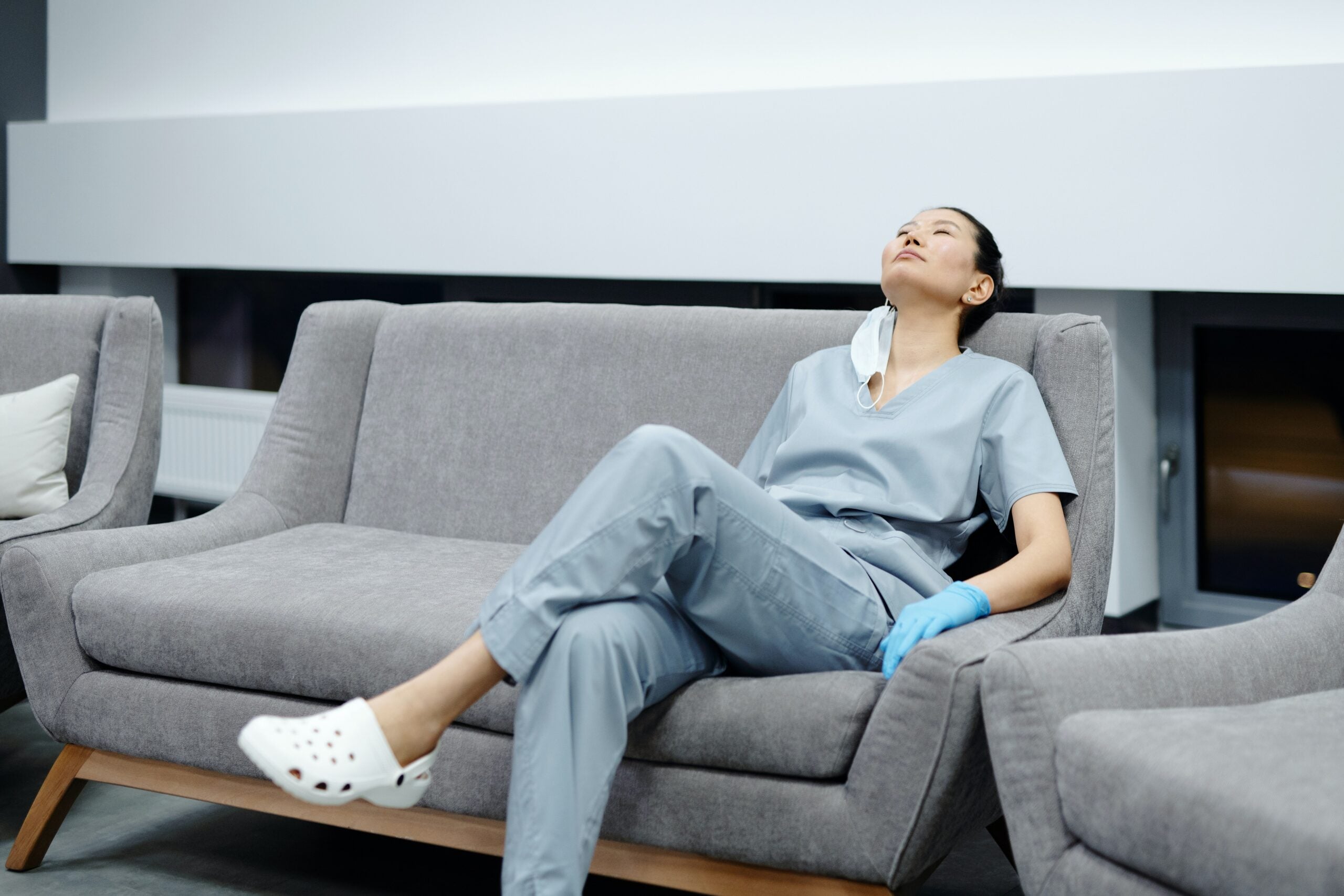 Asian woman medical care worker rests on a gray sofa.