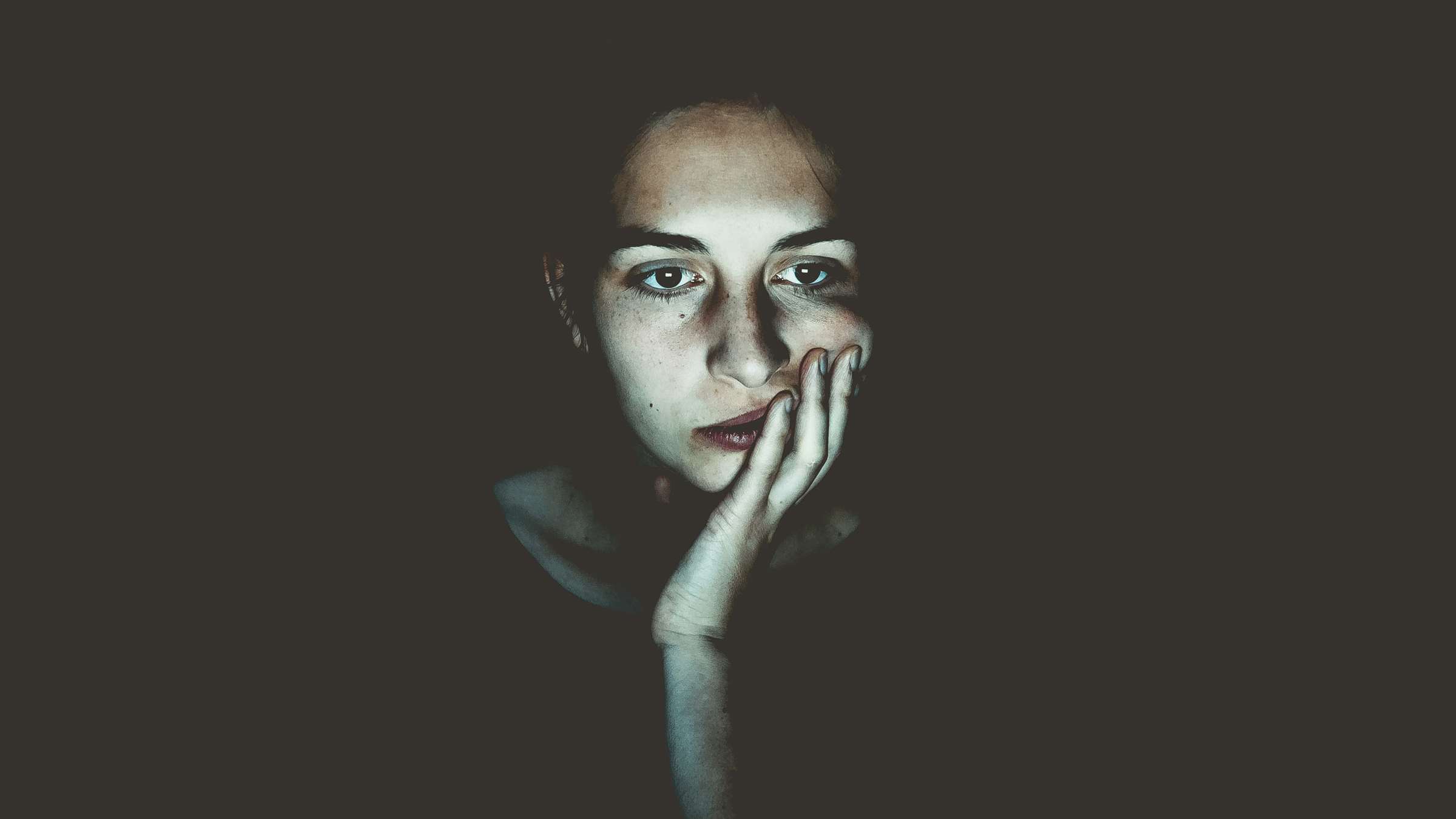 Woman staring at a computer screen in the dark while looking worried and emotionally exhausted