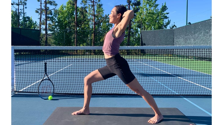 A person demonstrates a variation of Warrior 1 in yoga on the tennis court