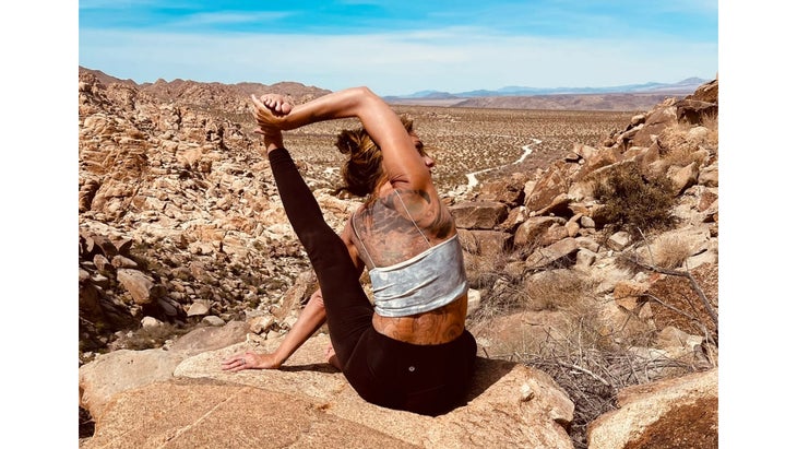 A woman practices Compass Pose in yoga on a rocky landscape