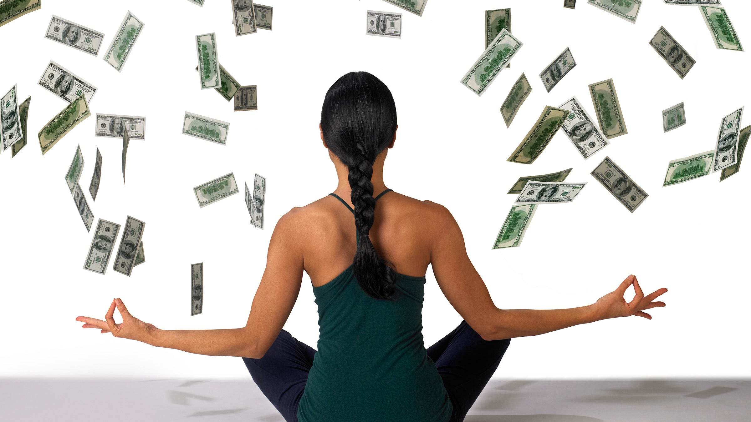 A woman sits in meditation posture while money falls from the sky