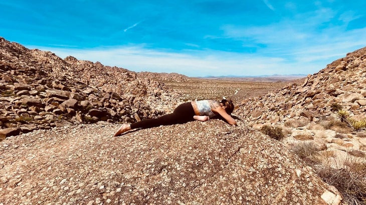 A woman practices One-Legged King Pigeon in yoga in a rocky landscape
