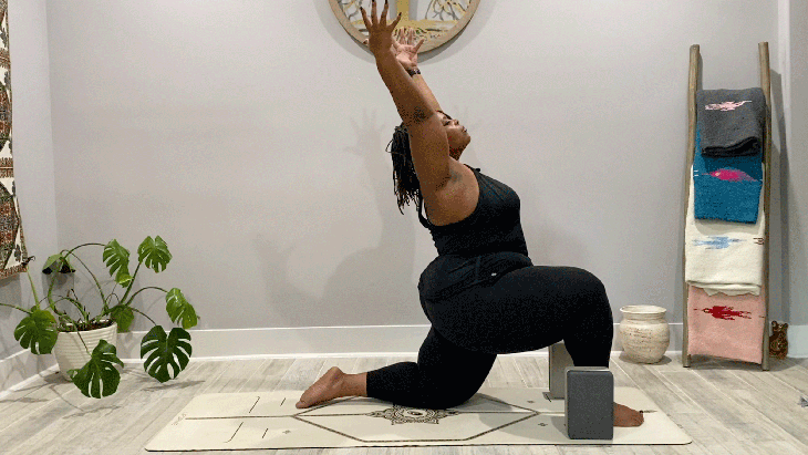 Woman in low lunge on her mat with her arms alongside her ears on a yoga mat
