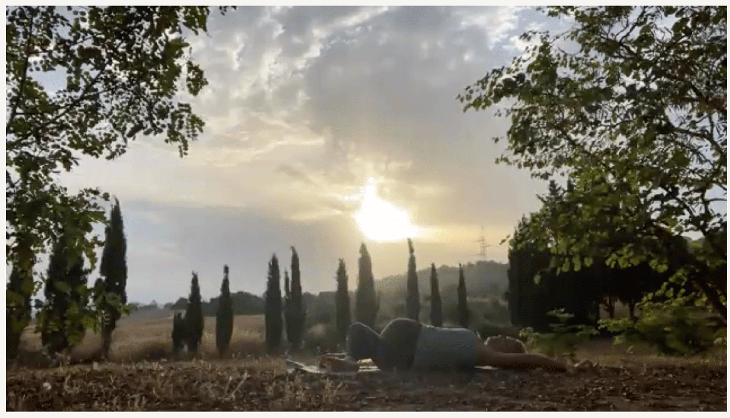 Woman practicing early morning yoga in a reclining twist outside at sunrise