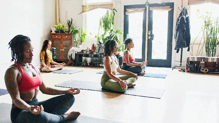 Women sitting cross-legged on their yoga mats in Sukhasana during a yoga class