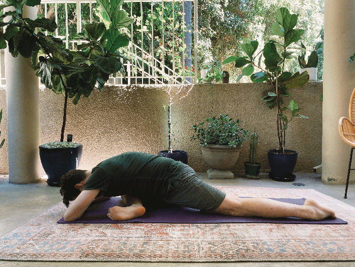 Man lying on his yoga mat with one knee bent and the other straight in Pigeon Pose