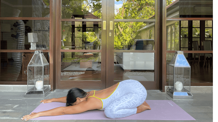 Woman in Child's Pose in her yoga mat with their hips near her heels and her arms extended forward to stretch her upper back and shoulders